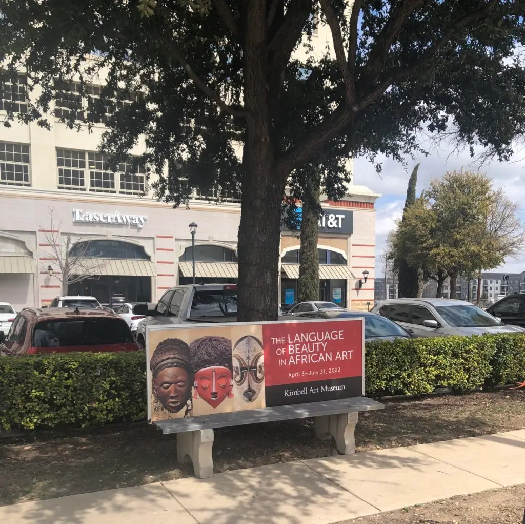 A bench in Fort Worth that has an advertisement on it for The Language of Beauty in African Art exhibit at the Kimbell Art Museum