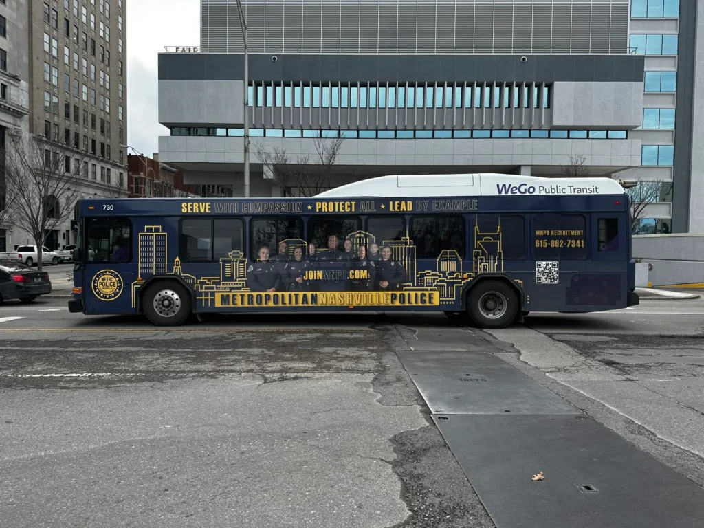 A Nashville Metro bus fully wrapped in navy and yellow promoting employment opportunities with the Metro Police.