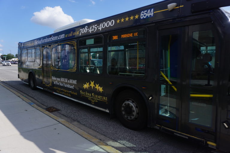 A fully wrapped Pace bus with Five Star Furniture's advertising on both sides and the back. The bus is pulling up to the sidewalk.