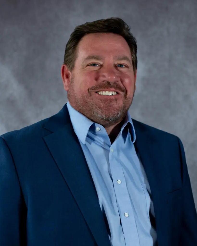 A headshot of Jason Klare. He is wearing a blue button down shirt, with a navy blazer.